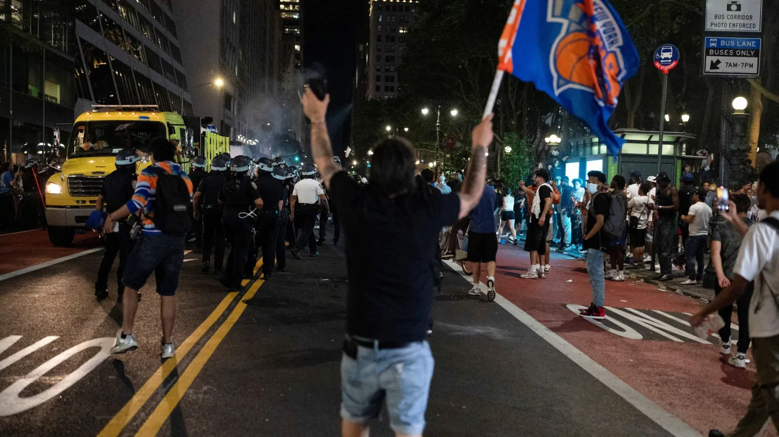 REUTERS/Christian Monterrosa Man walks down a New York street away from the camera holding a Knicks flag with his arms up and a crowd around